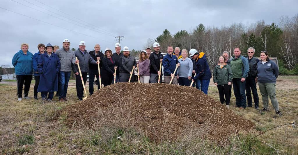 A group of people with shovels stand behind a pile of dirt.