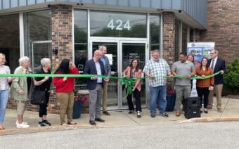A group of people cutting a ribbon outside of a building.