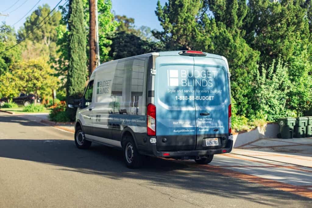 A van is driving down a street with trees and bushes.