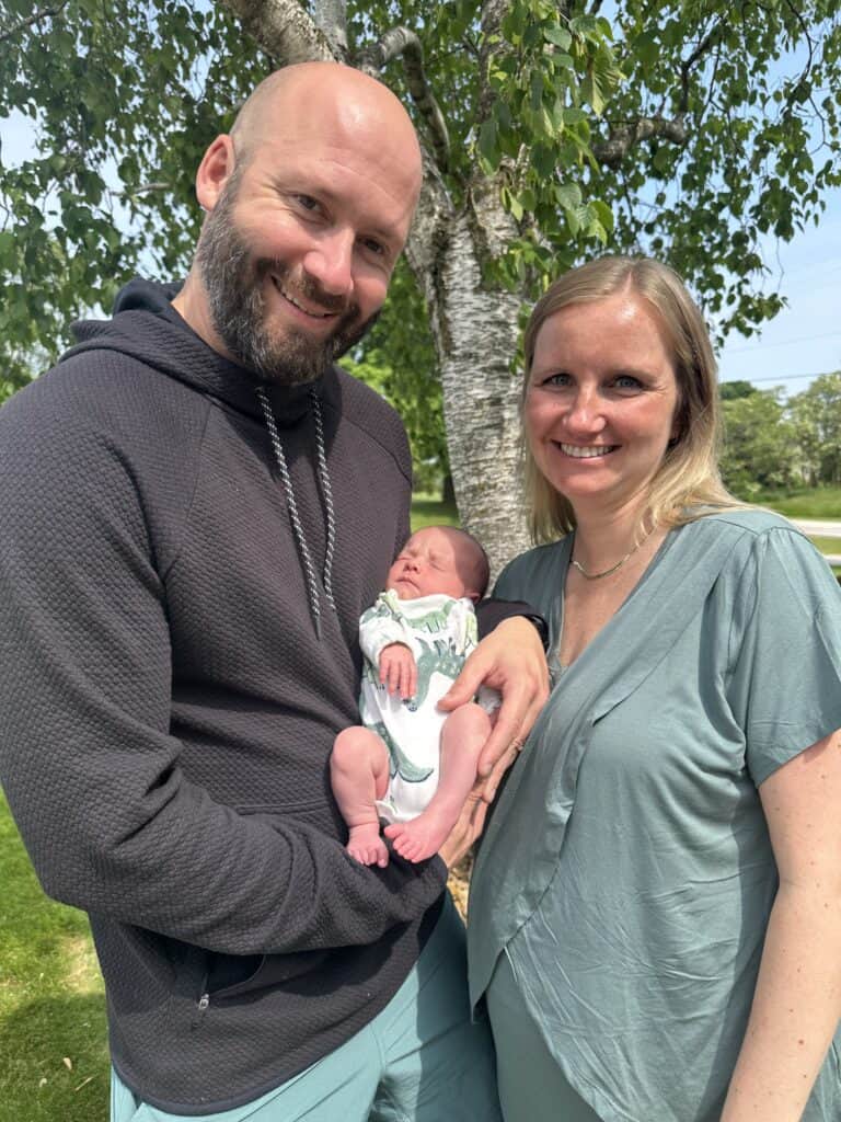 A man and woman holding a baby in front of a tree.