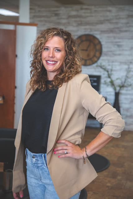 A woman in a salon wearing a blazer and jeans.