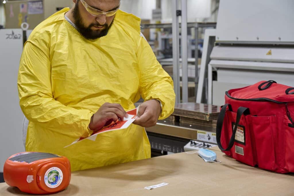 A man in a yellow lab coat peeling a sticker.