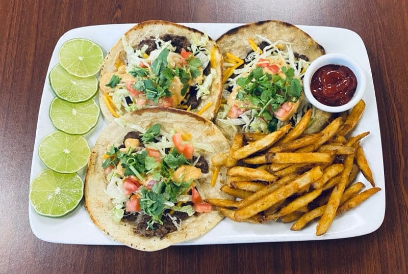Three tacos and french fries on a white plate.