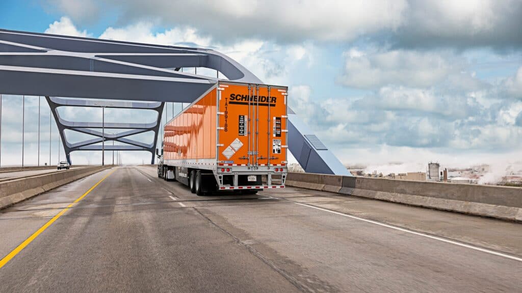 A large orange truck driving on a bridge.
