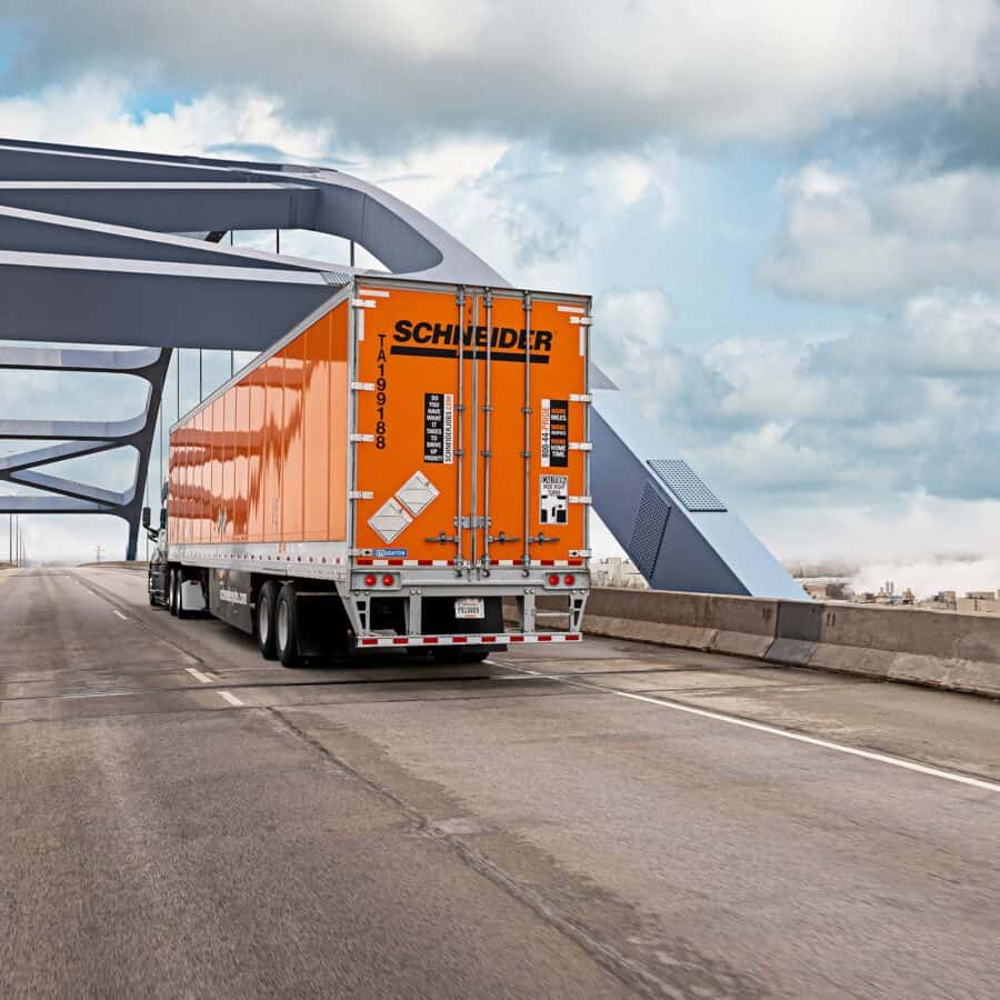 A large orange truck driving on a bridge.