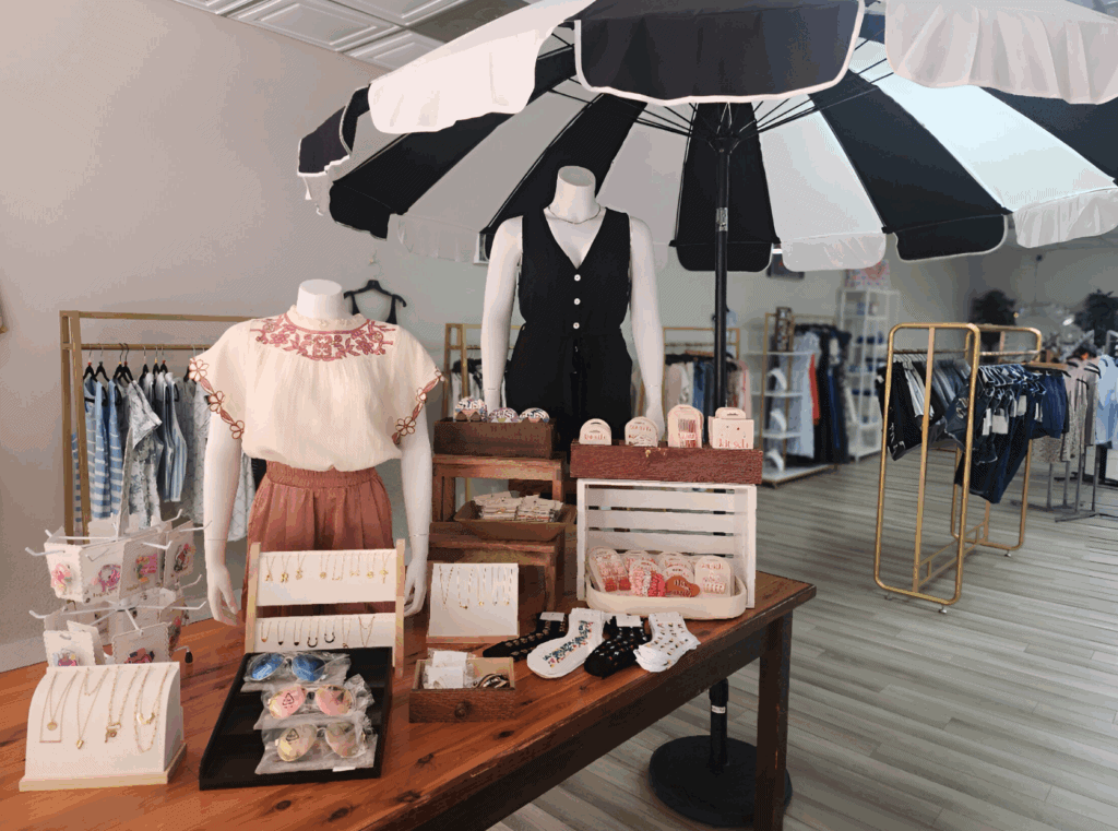 A table with clothes and accessories under an umbrella.