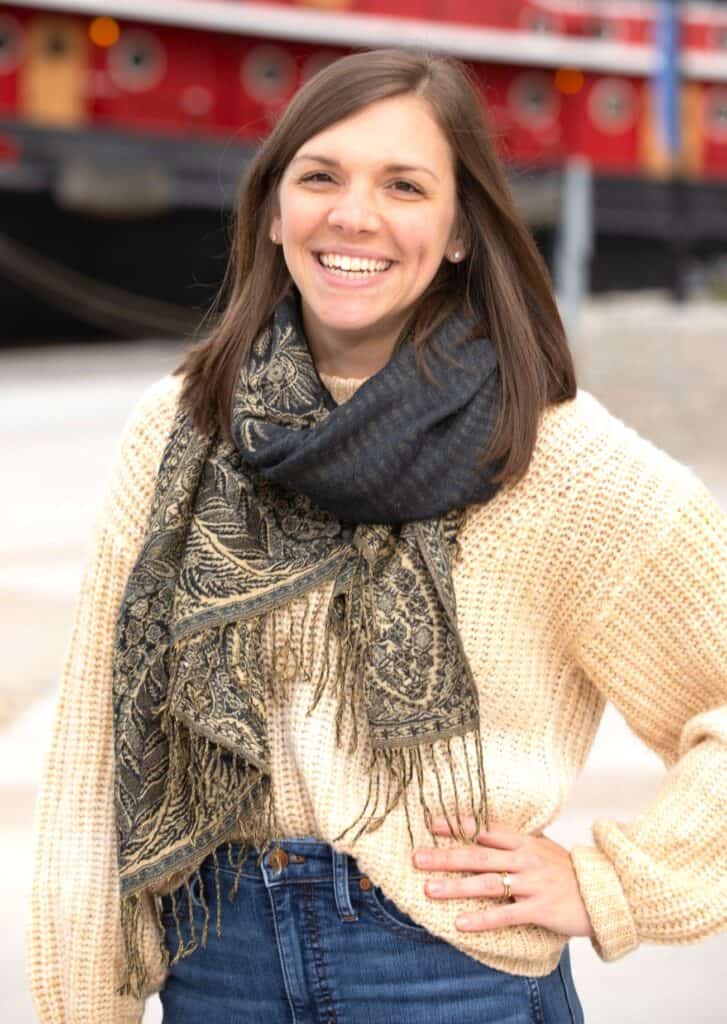 A woman wearing a scarf and jeans standing in front of a boat.