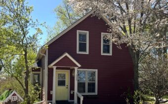 A red house with a white door and a tree in front of it.