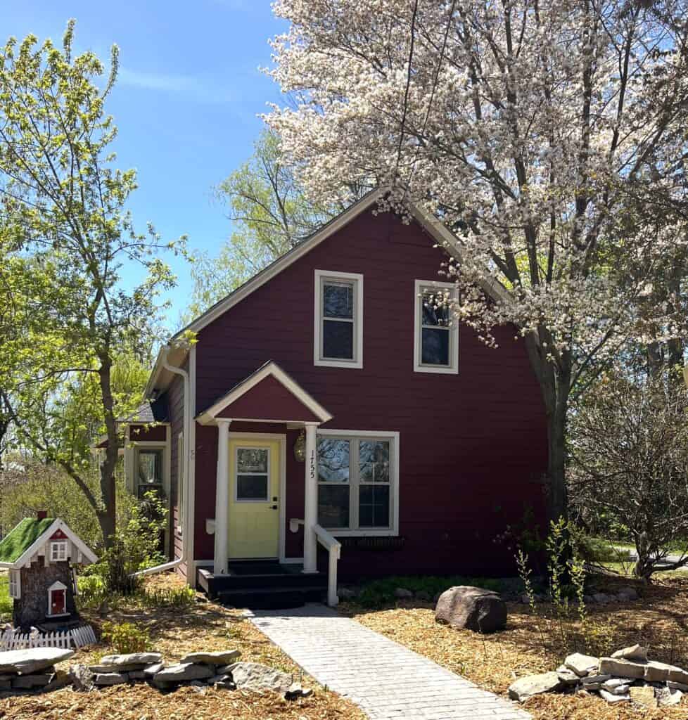 A red house with a white door and a tree in front of it.