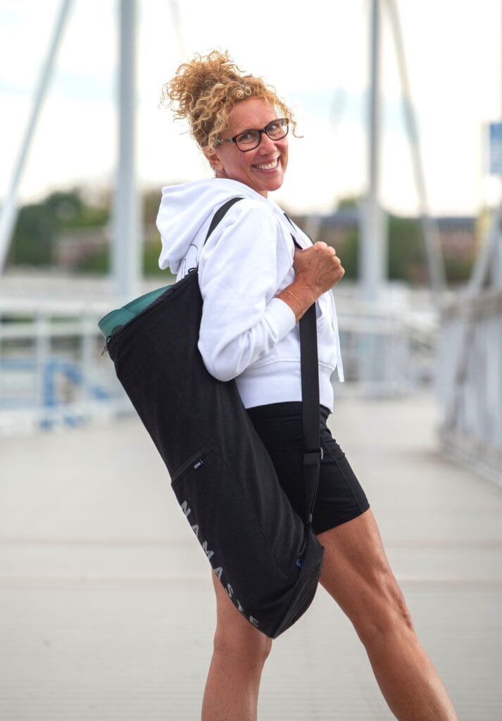 A woman with glasses and a backpack is walking on a bridge.