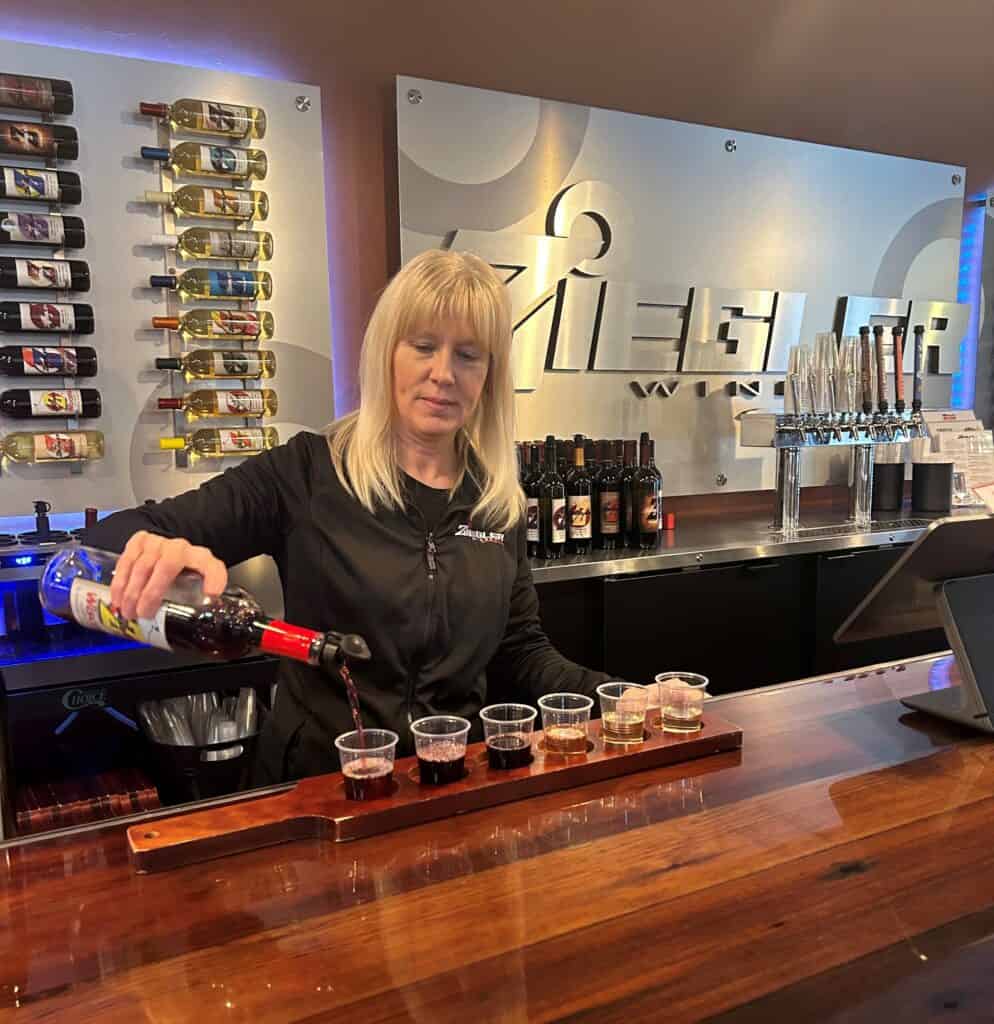 A woman pouring wine into glasses at a bar.